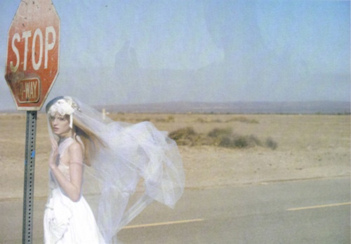 a woman in a wedding dress standing next to a stop sign with a veil on her head