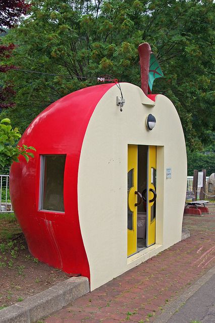 a large red and white apple shaped building on the side of a road with trees in the background