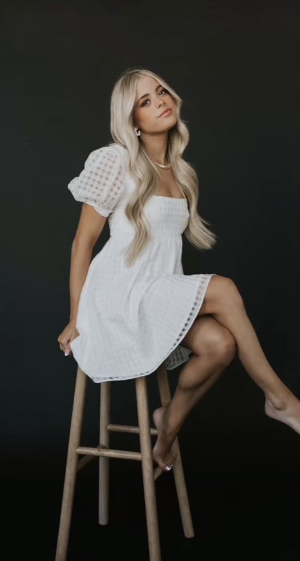 a woman sitting on top of a wooden stool wearing a white dress and high heels