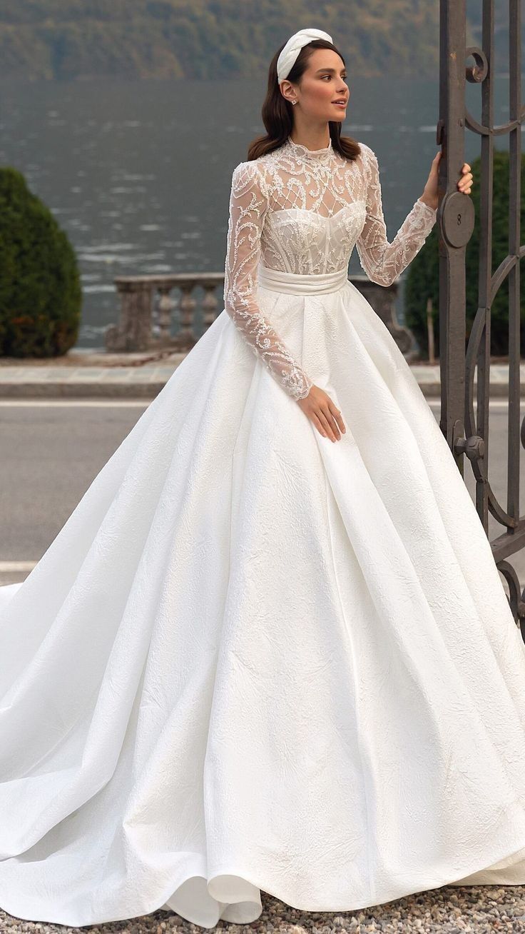 a woman in a white wedding dress standing next to a gate and looking off into the distance