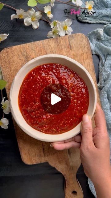 a person holding a bowl of sauce on top of a wooden cutting board