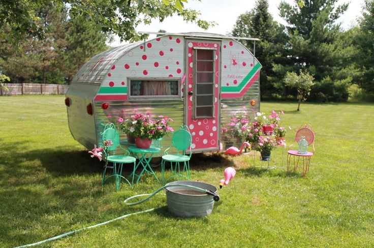 an old trailer is decorated with flowers and potted plants in the back yard area