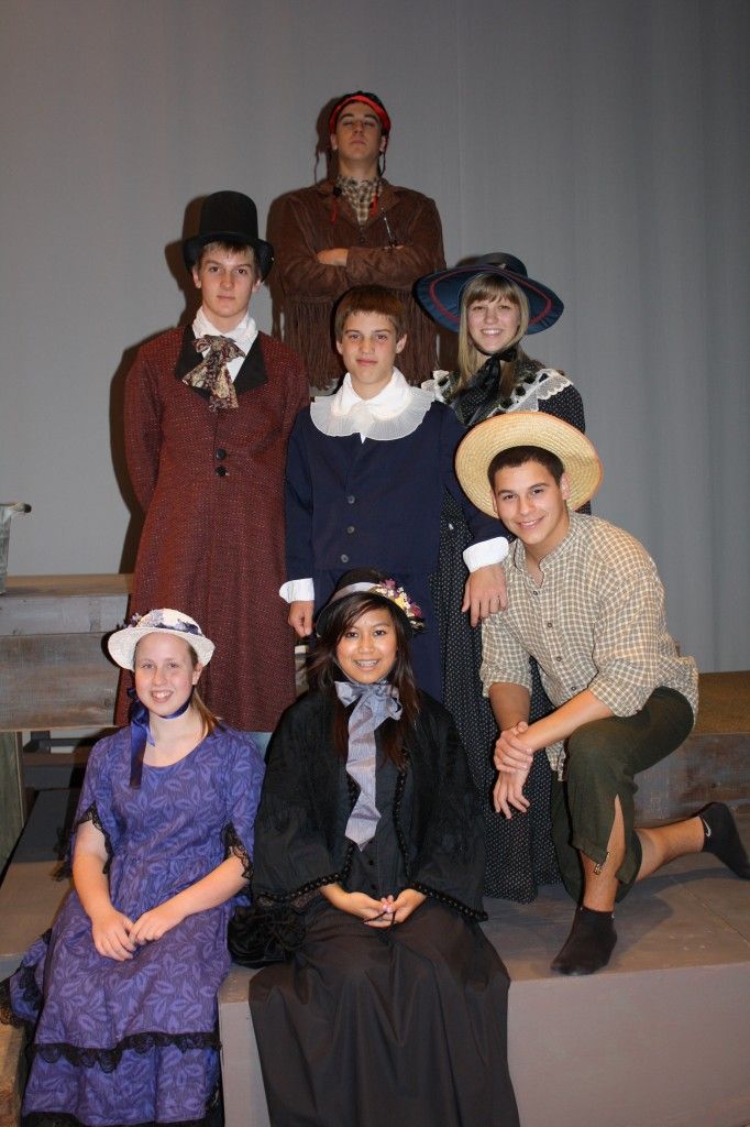 a group of people in period costumes posing for a photo with one woman sitting on a bench