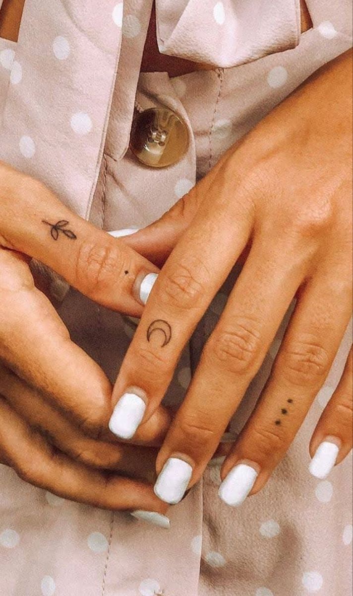 two hands holding each other with small tattoos on their thumbnails and one finger