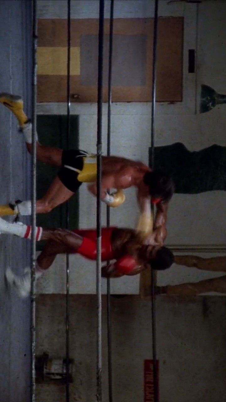 two men are boxing in the ring with ropes hanging from the ceiling and one man is wearing red shorts