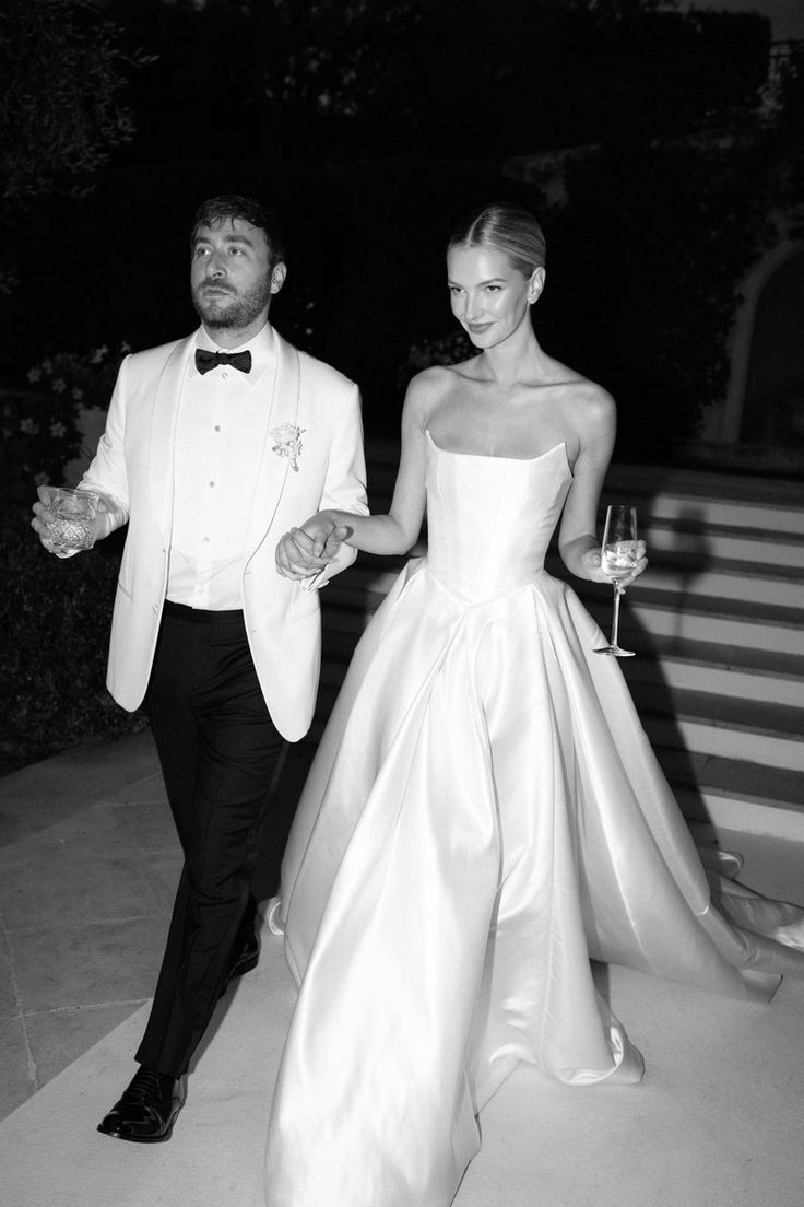 a man in a tuxedo walking next to a woman in a gown holding hands