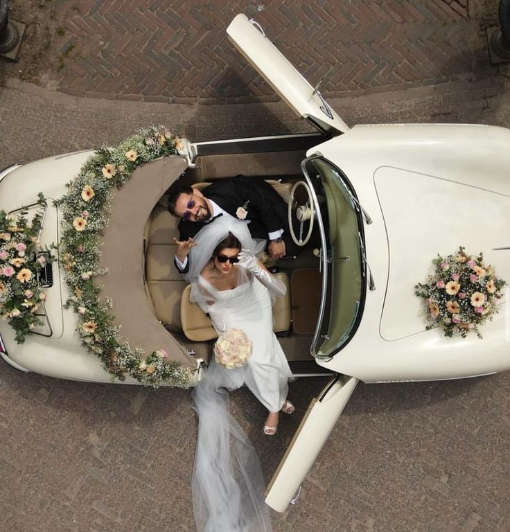 a bride and groom are in the back of a white car with flowers on it