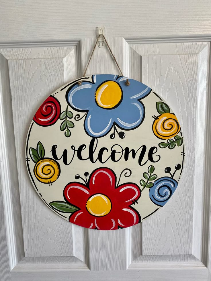 a welcome sign hanging on a door with flowers and swirls painted on the front