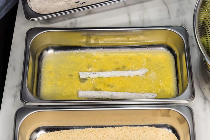 three metal trays filled with food sitting on top of a white marble countertop