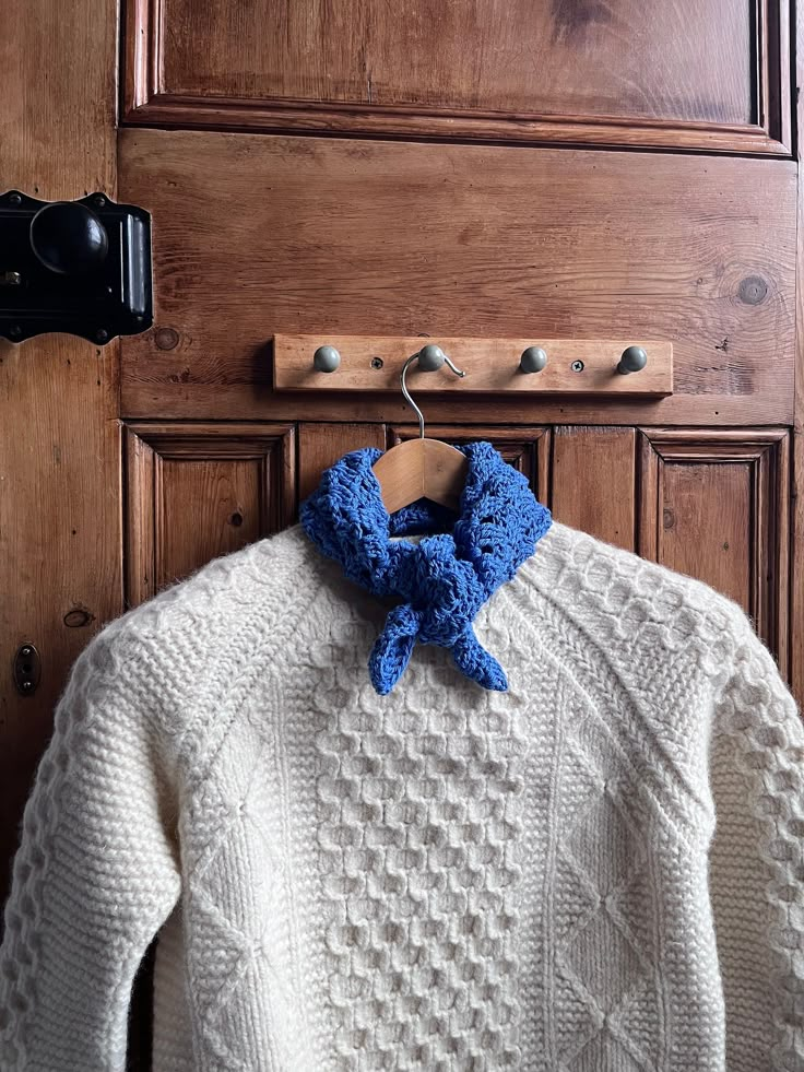 a white sweater with a blue bow is hanging on a coat rack in front of a wooden door