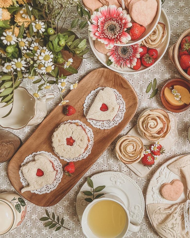 desserts and pastries are arranged on a table with flowers, teacups and plates