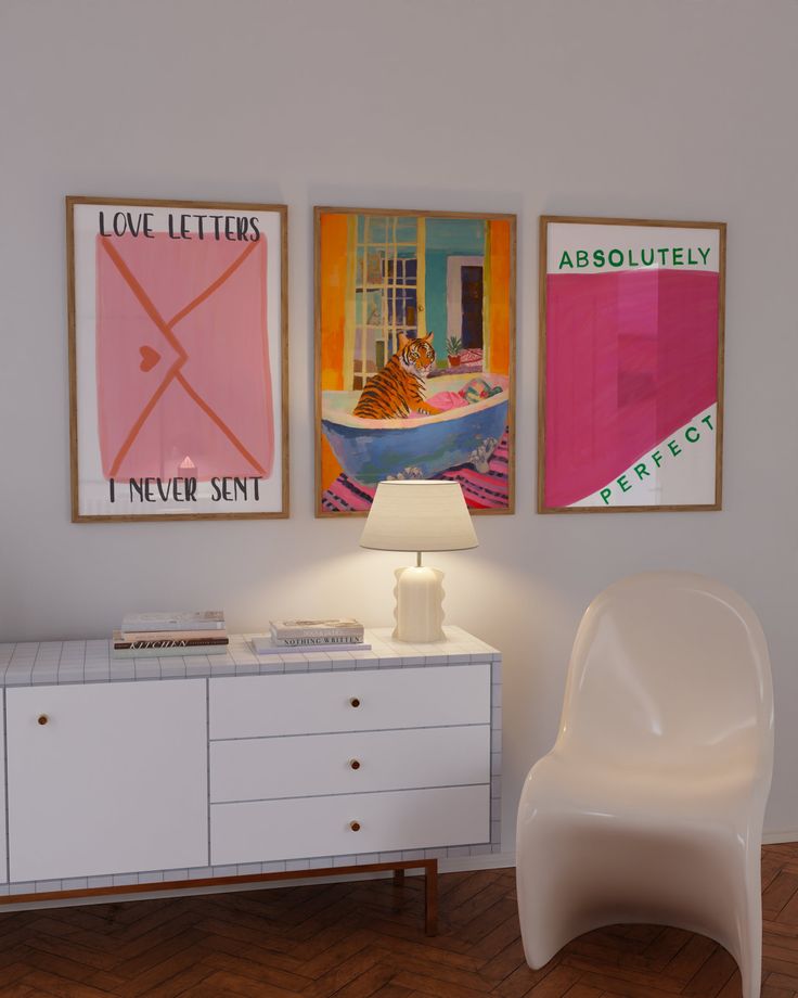 there are two pictures on the wall next to a white chair and a table with a lamp