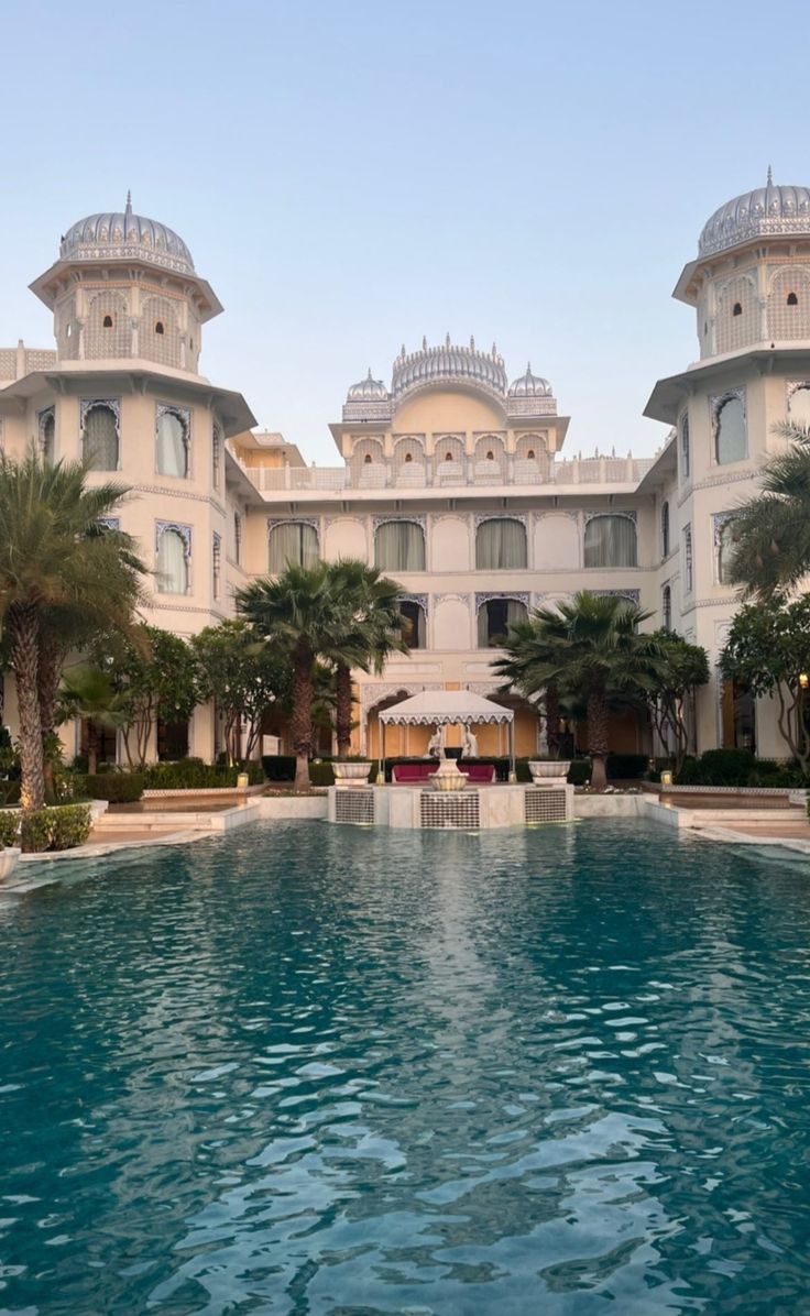 an outdoor swimming pool in front of a large white building with palm trees around it