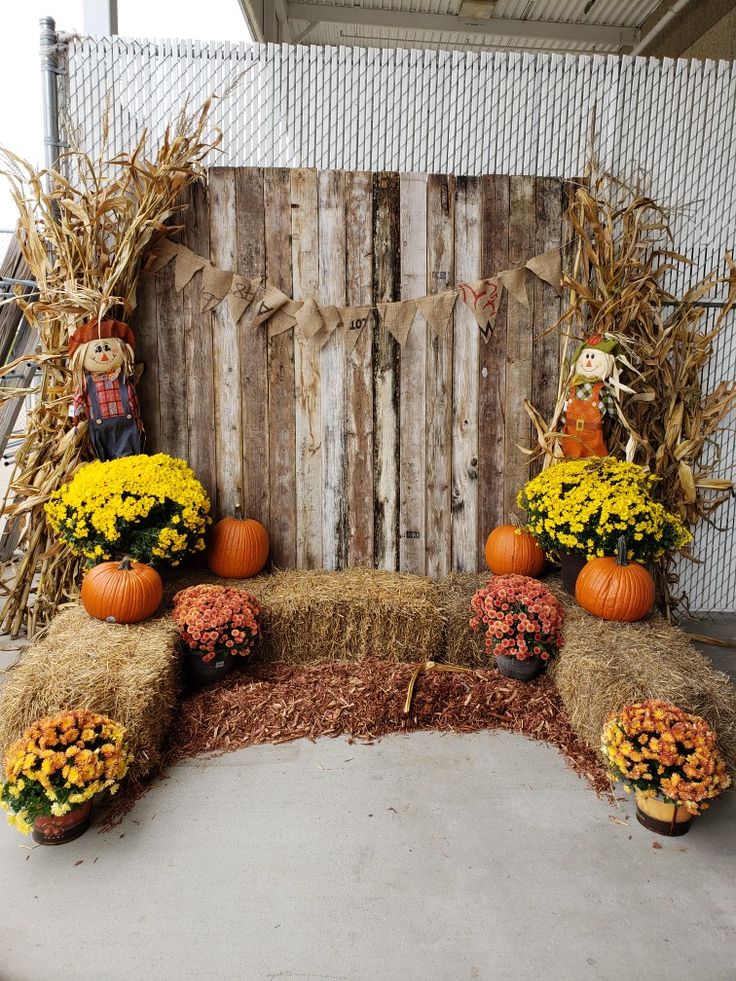 an arrangement of pumpkins, hay and flowers on display in front of a wooden fence