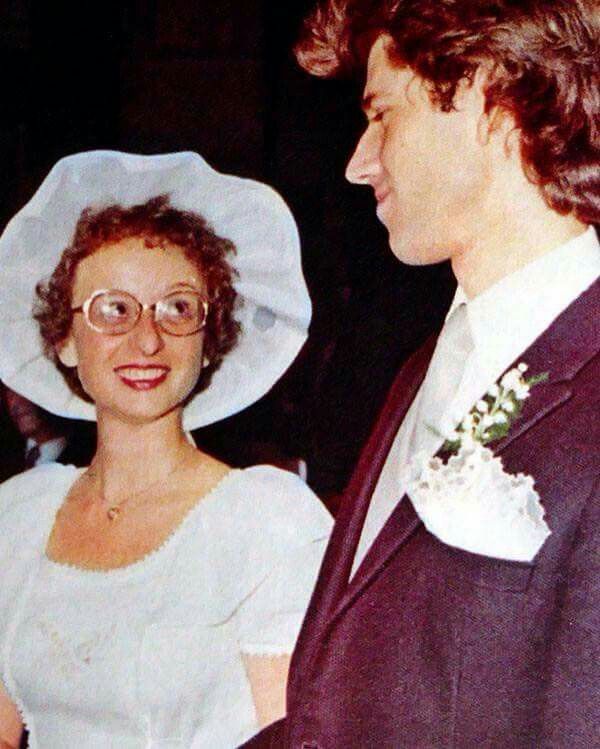 a man in a suit and tie standing next to a woman wearing a white hat