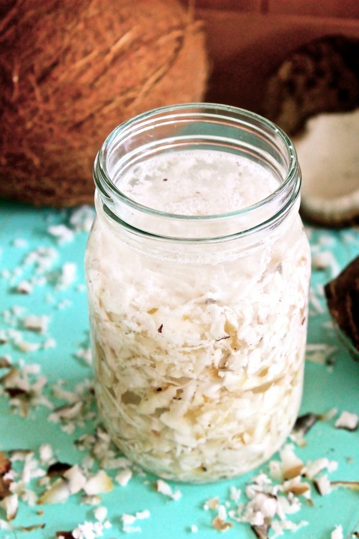 coconut milk in a glass jar next to an unpeeled coconut on a blue surface