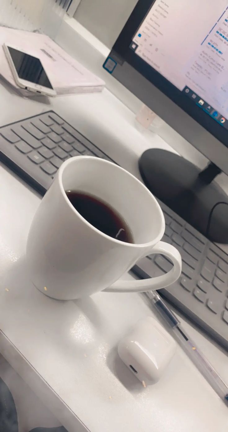 a cup of coffee sitting on top of a white desk next to a computer keyboard