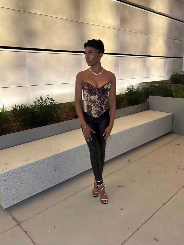 a woman standing in front of a wall with plants on it and wearing black leather pants