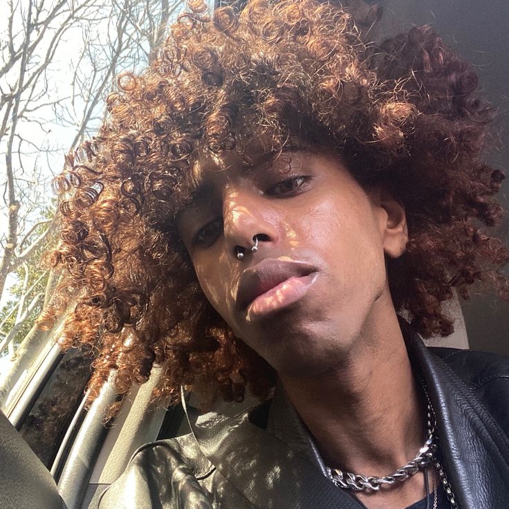 a close up of a person in a car with an afro haircut and necklace