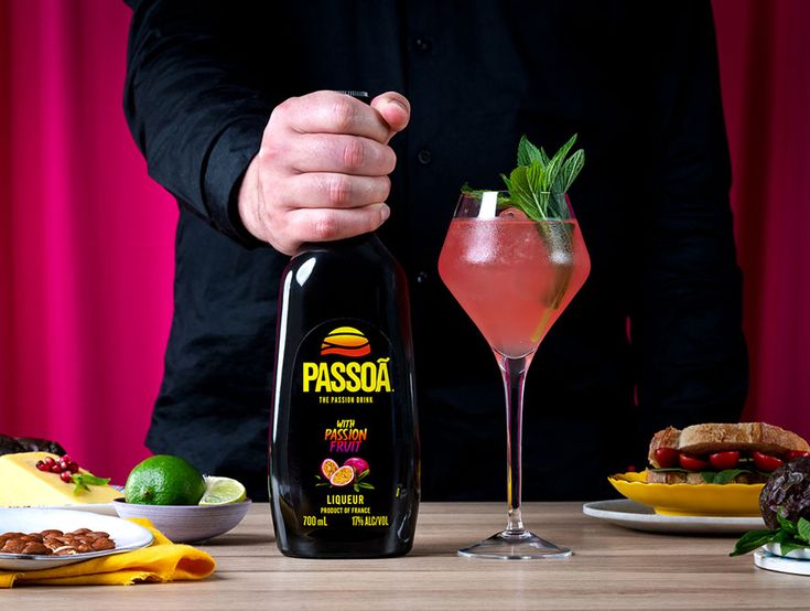 a man holding a bottle of passosa next to a glass filled with pink liquid