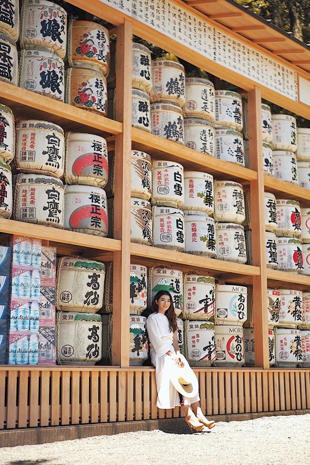 a woman sitting on the side of a building next to stacks of barrels and cans