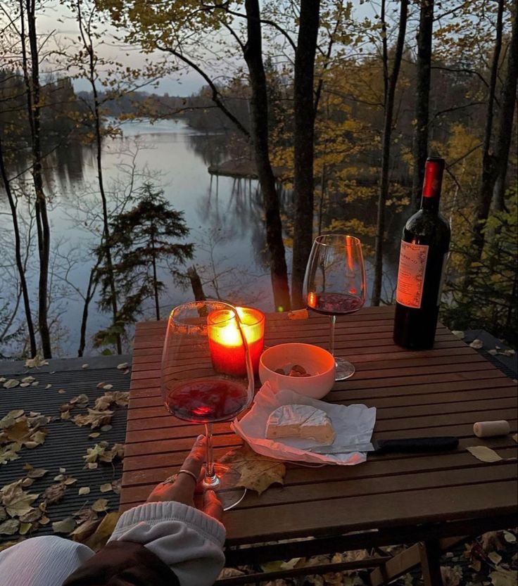 two glasses of wine are sitting on a table with food and candles in front of the water