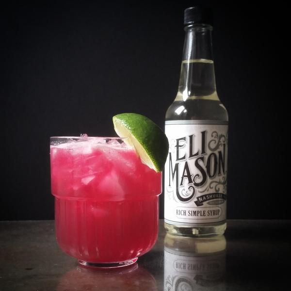 a pink drink with a lime garnish next to a bottle