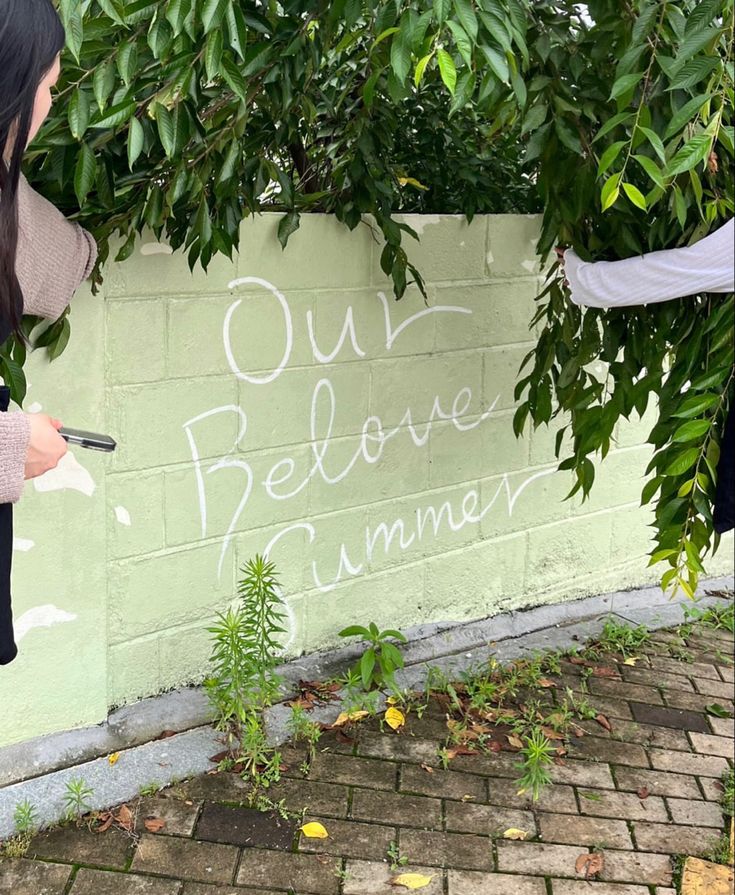 two girls are writing on the side of a wall with trees in front of them