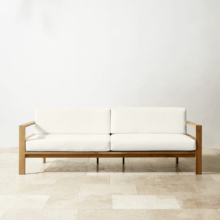 a white couch sitting on top of a tile floor next to a wall with a wooden frame