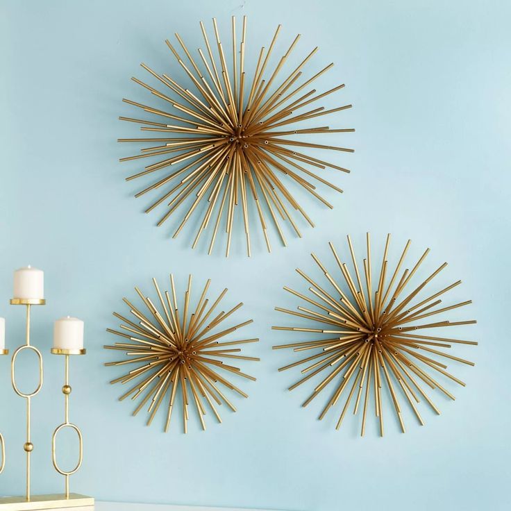 three gold starburst wall art pieces on a blue wall next to two candles