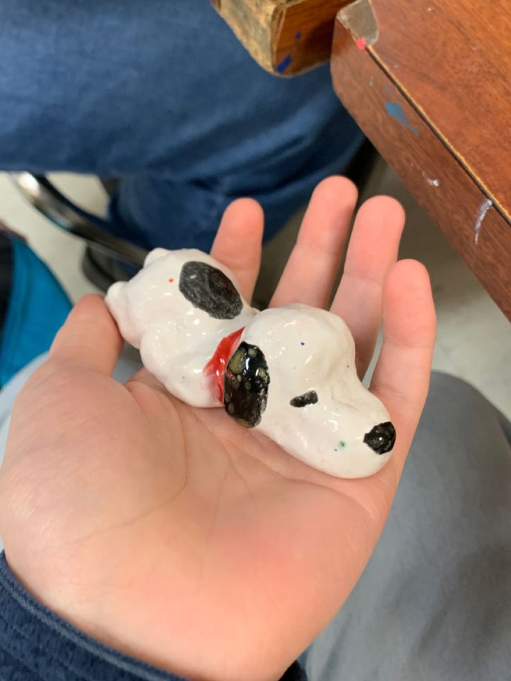 a hand holding a small white dog figurine in it's left palm