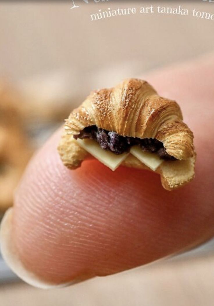 a tiny croissant is sitting on someone's finger and has cheese in it