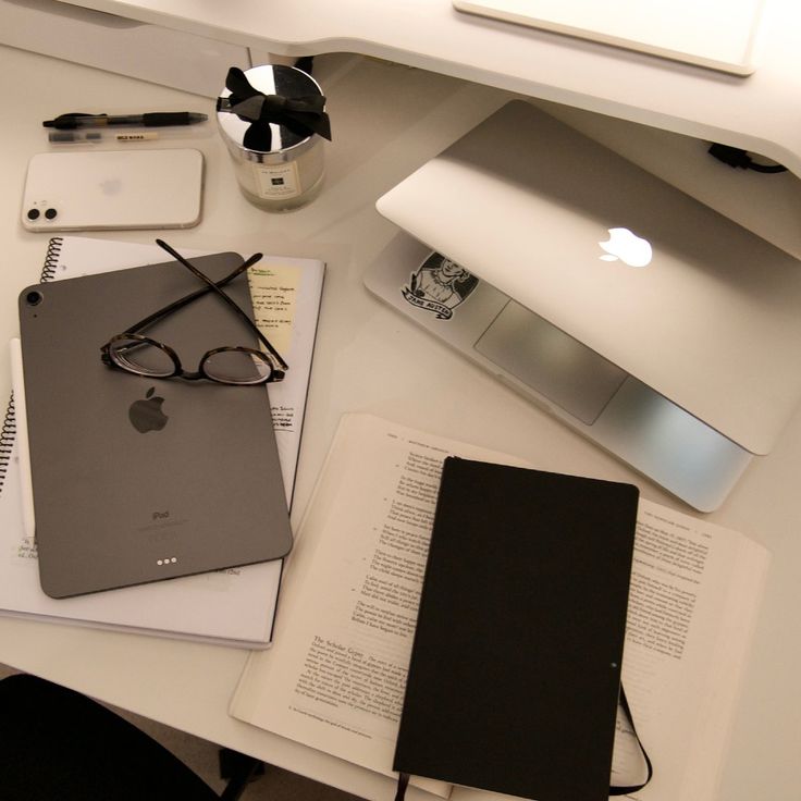 an apple computer sitting on top of a desk next to a notebook and pen with glasses