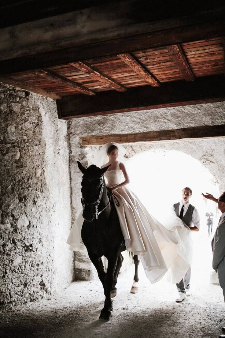 a woman riding on the back of a black horse in a stone walled area next to two men