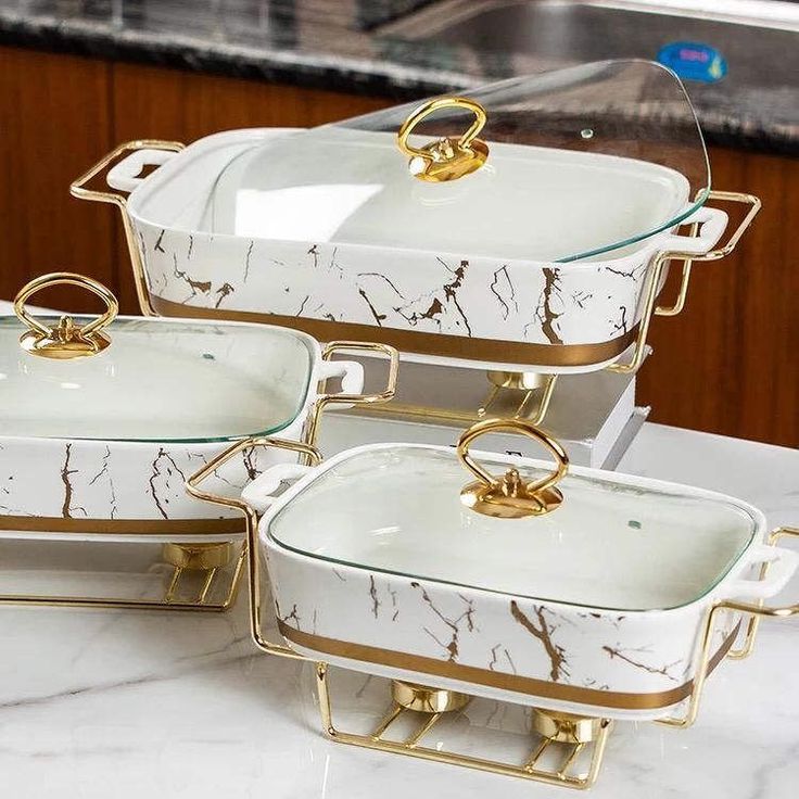 three white and gold dishes sitting on top of a marble counter