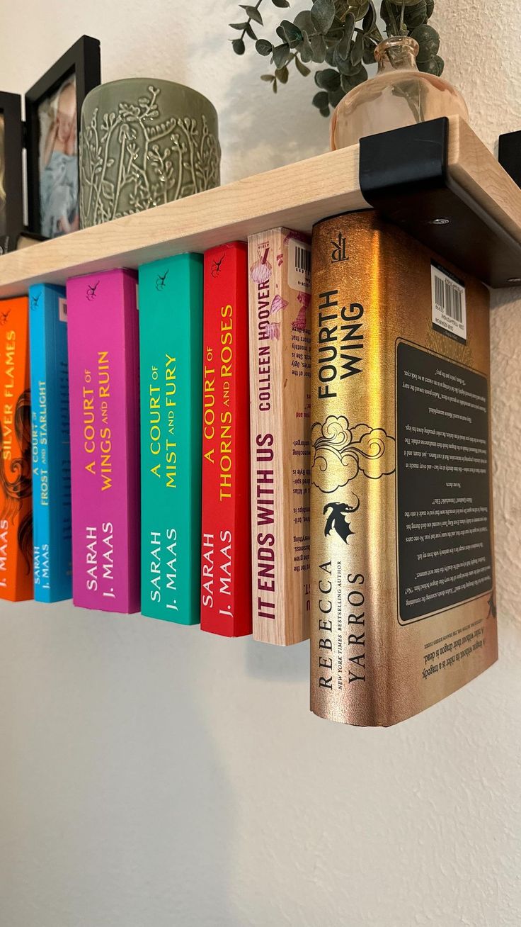 a row of books sitting on top of a wooden shelf next to a potted plant