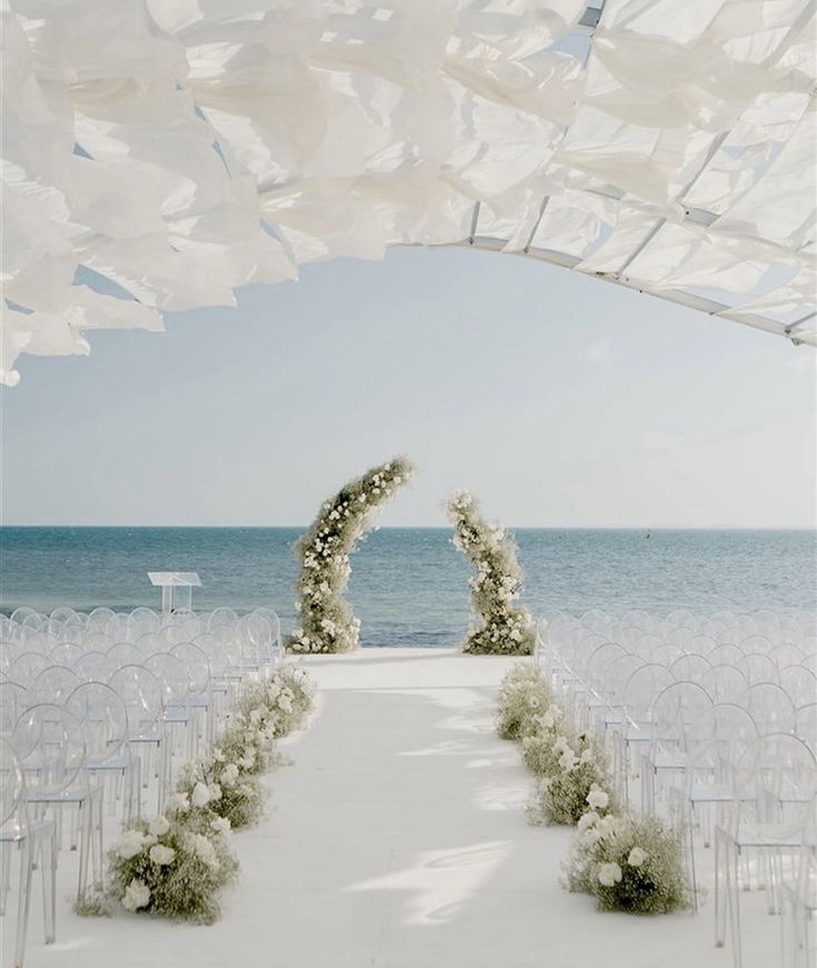 an outdoor ceremony setup with white chairs and flowers on the aisle, overlooking the ocean