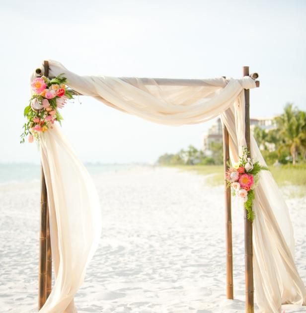 an outdoor ceremony setup on the beach with white draping and pink flower arrangements