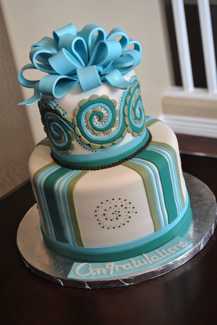 a three tiered cake decorated with blue and green ribbons on top of a wooden table