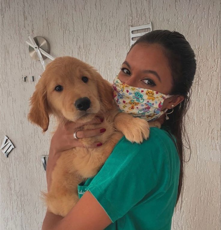 a woman wearing a face mask holding a dog in front of a wall with clocks on it