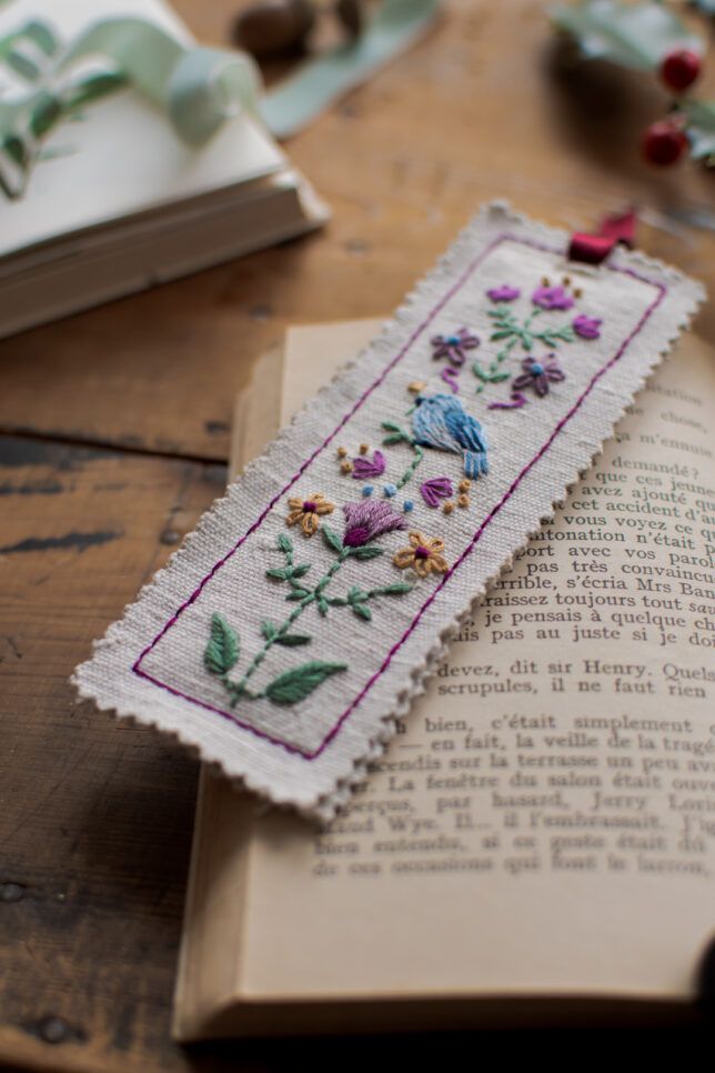 a bookmark with flowers on it sitting on top of a table next to an open book