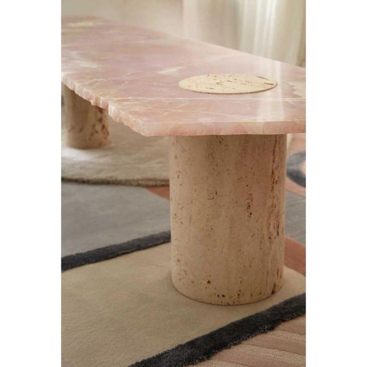 a table made out of stone with a circular base on it's end, sitting in front of rugs