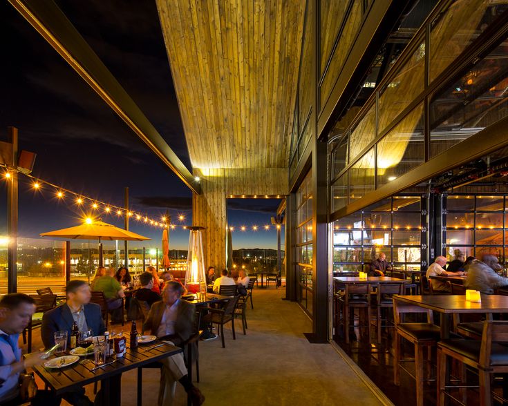 people sitting at tables in a restaurant with lights on the ceiling and wooden beams above them