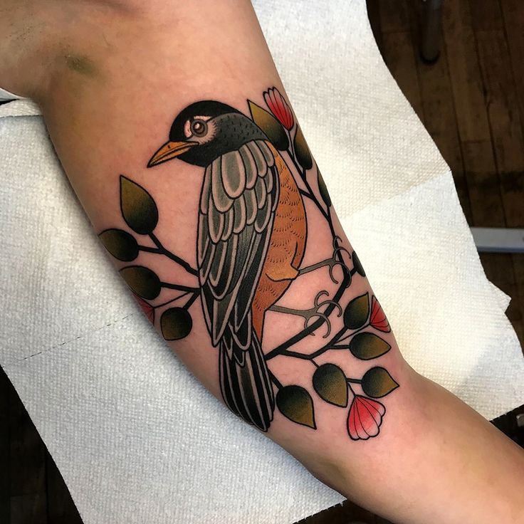 a bird sitting on top of a branch with leaves and flowers around its neck tattoo