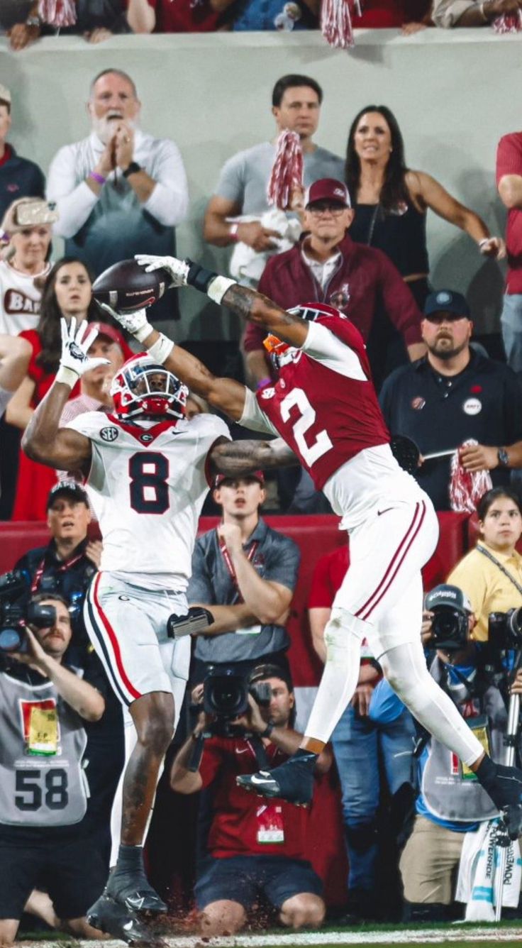 two football players jumping up in the air to catch a ball while people watch from the stands