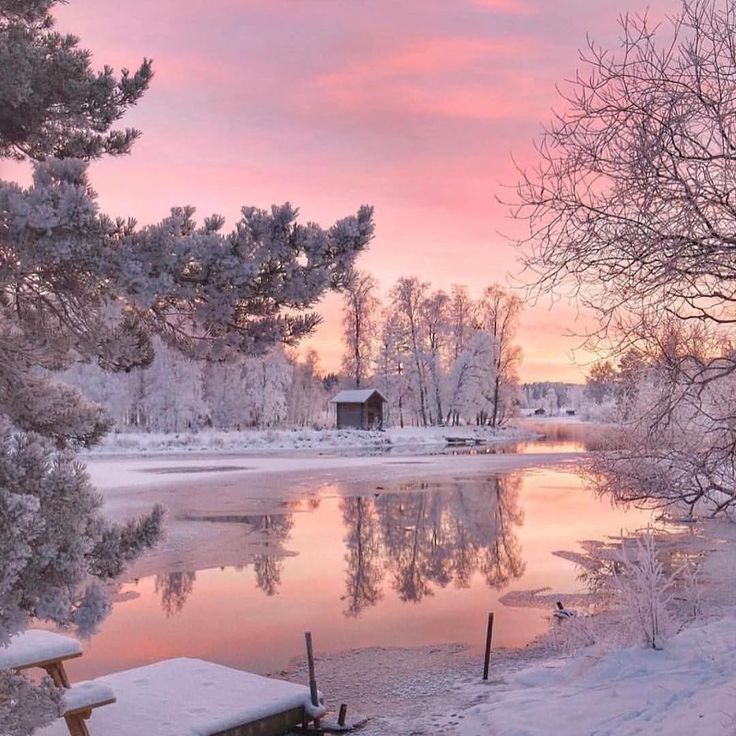 a lake with snow on the ground and trees in the foreground, at sunset