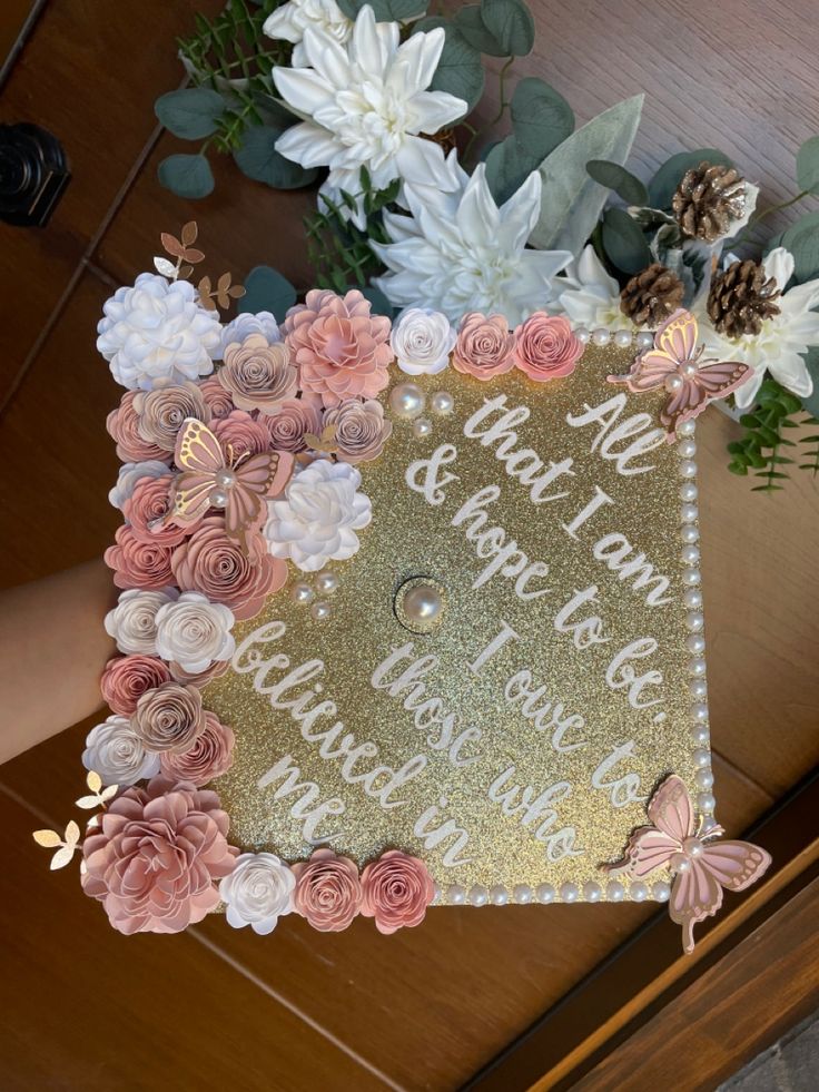 a graduation cap decorated with flowers on top of a wooden table next to white and pink flowers