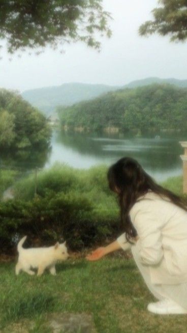 a woman kneeling down next to a white cat on top of a grass covered field