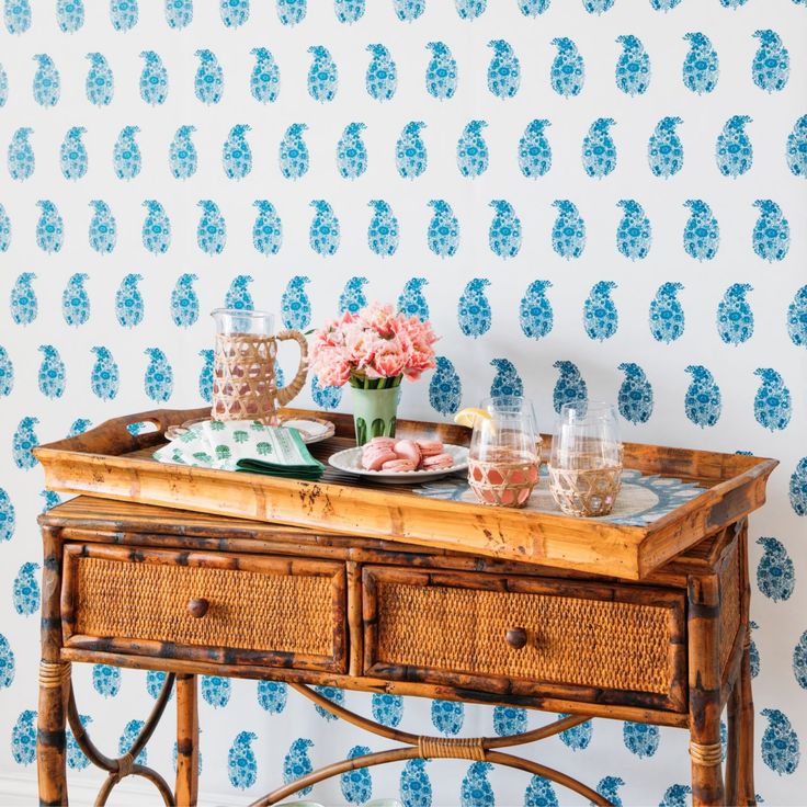 a wooden table topped with flowers next to a blue wallpapered wall behind it