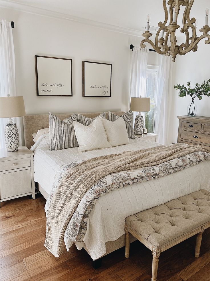 a bedroom with white walls and wood flooring has a chandelier hanging above the bed